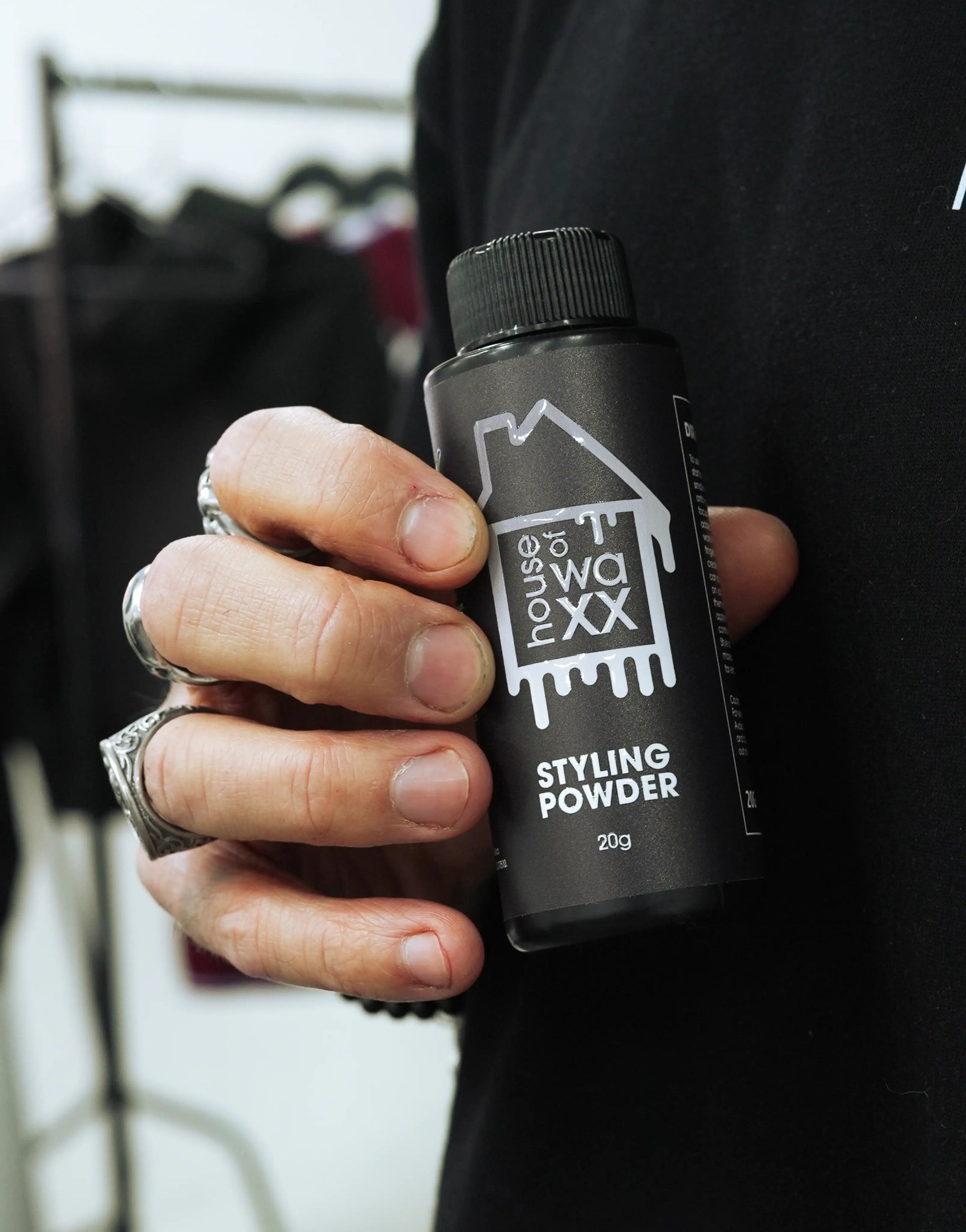Hand holding a bottle of House of Waxx Styling Powder in front of a black t-shirt