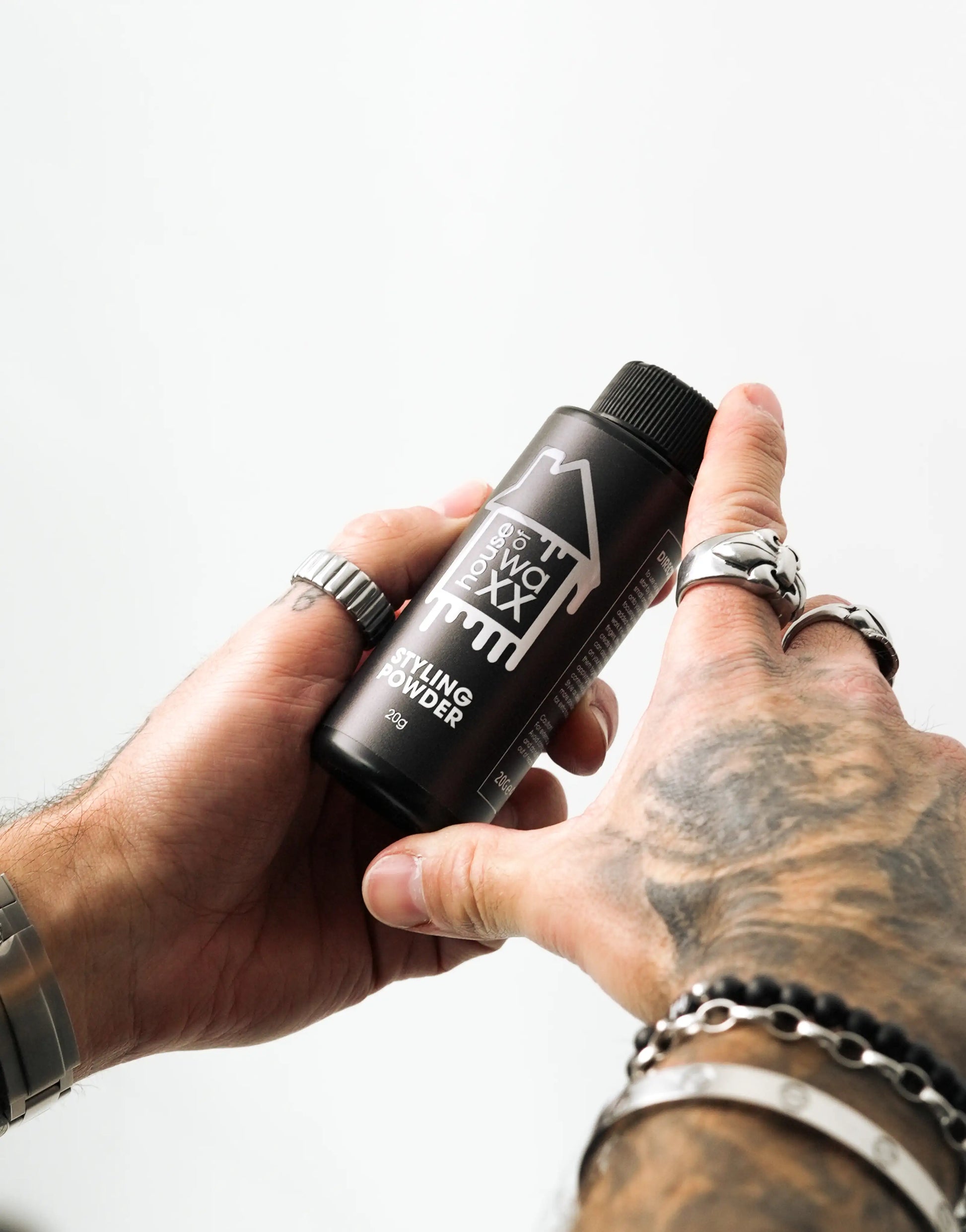 Tattooed man holding a bottle of House of Waxx Styling Powder, 20g, against a plain white background