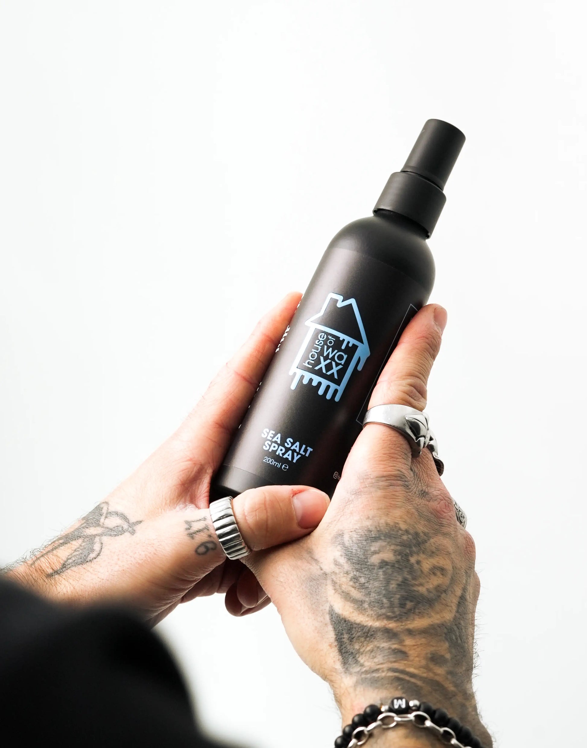 Tattooed man holding a bottle of House of Waxx Sea Salt Spray, 200ml, against a plain white background