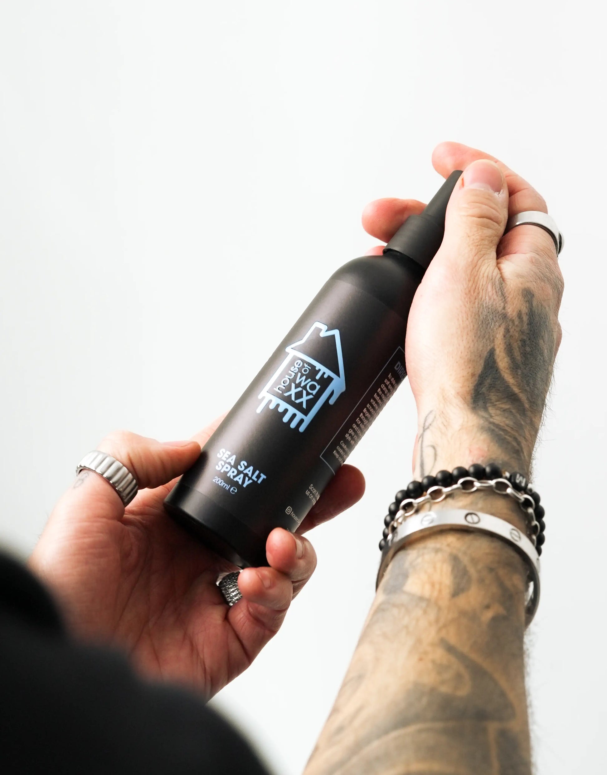 Tattooed man holding a bottle of House of Waxx Sea Salt Spray, 200ml, against a plain white background
